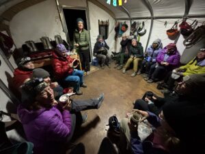 Women sitting in a circle inside a canvas hut eating breakfast at 4am